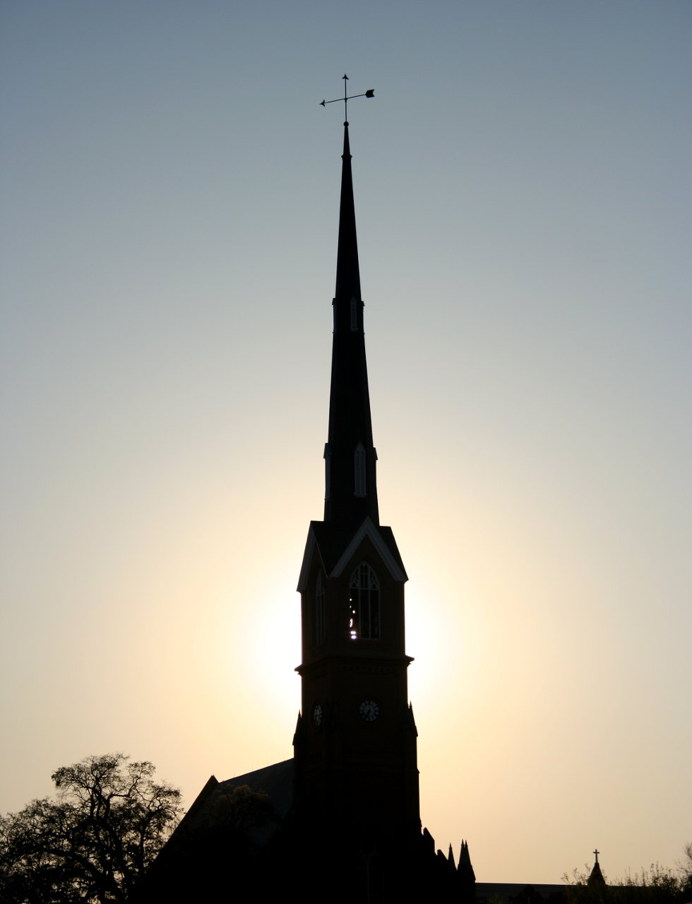 A church spire silhouetted against the sun