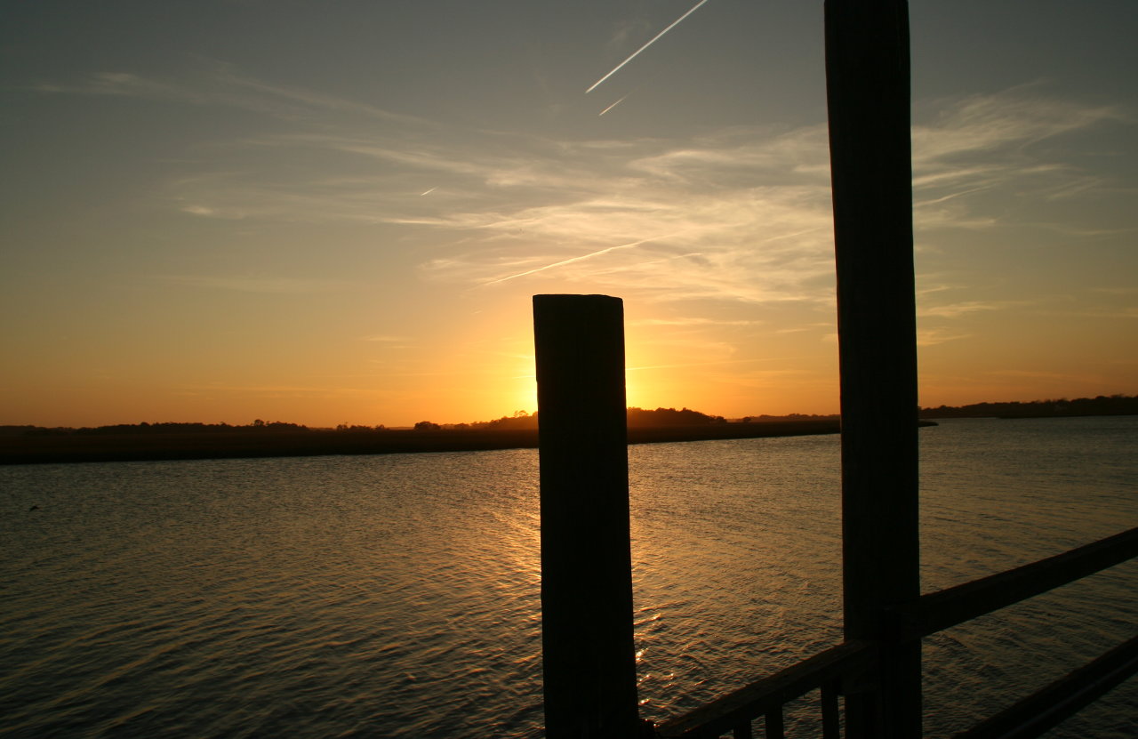 The post of a pier silhouetted against the setting sun.