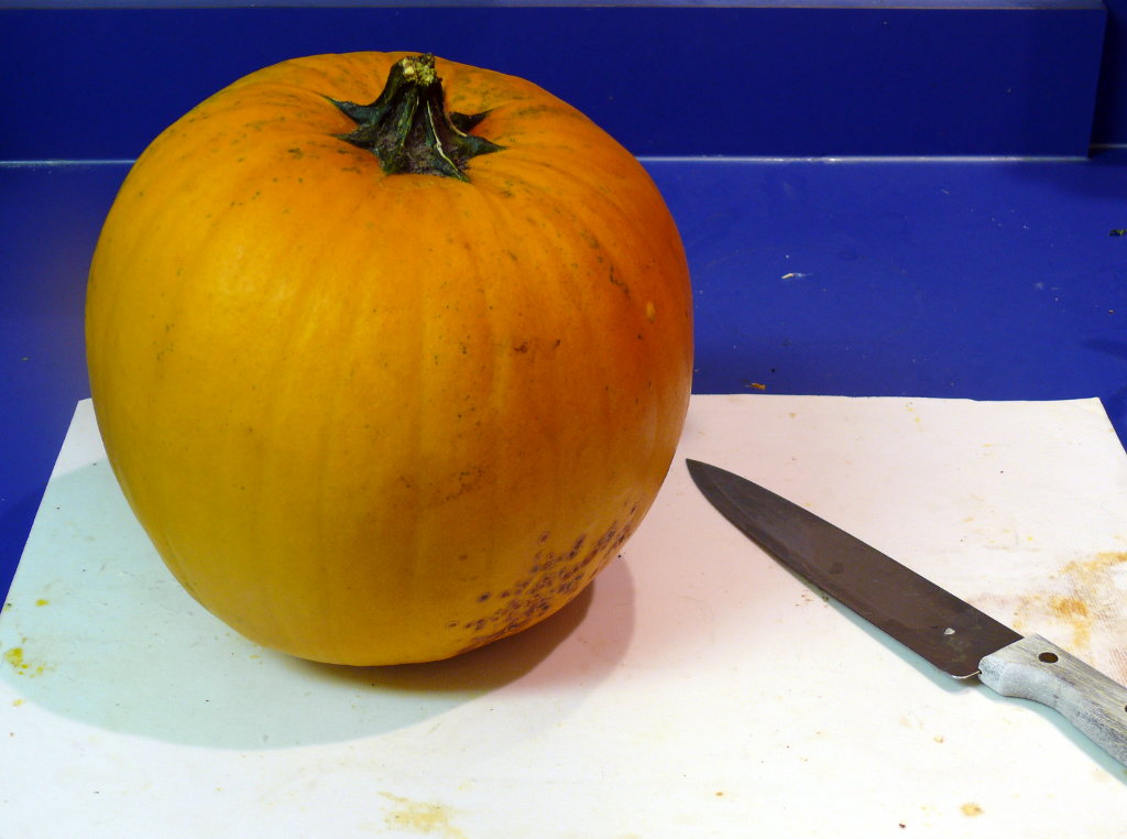 A whole pumpkin and knife on a cutting board