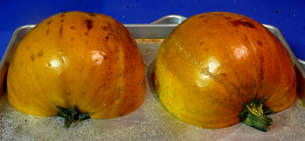 Two pumpkin halves with the cut side down on a sheet pan.