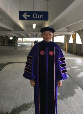 In my graduation regalia under the Out sign