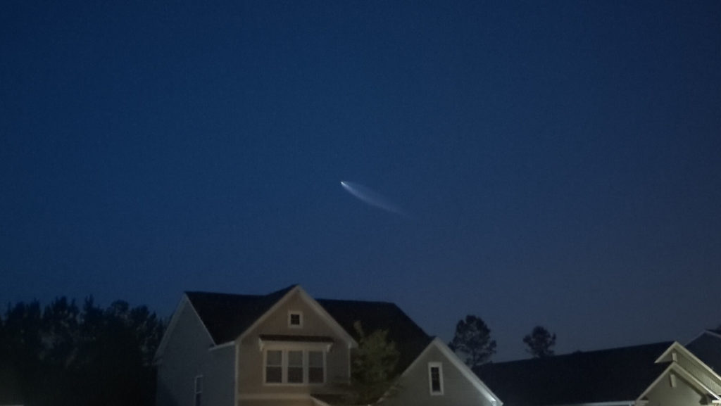 SpaceX Falcon 9 exhaust plume visible over some houses in the foreground.