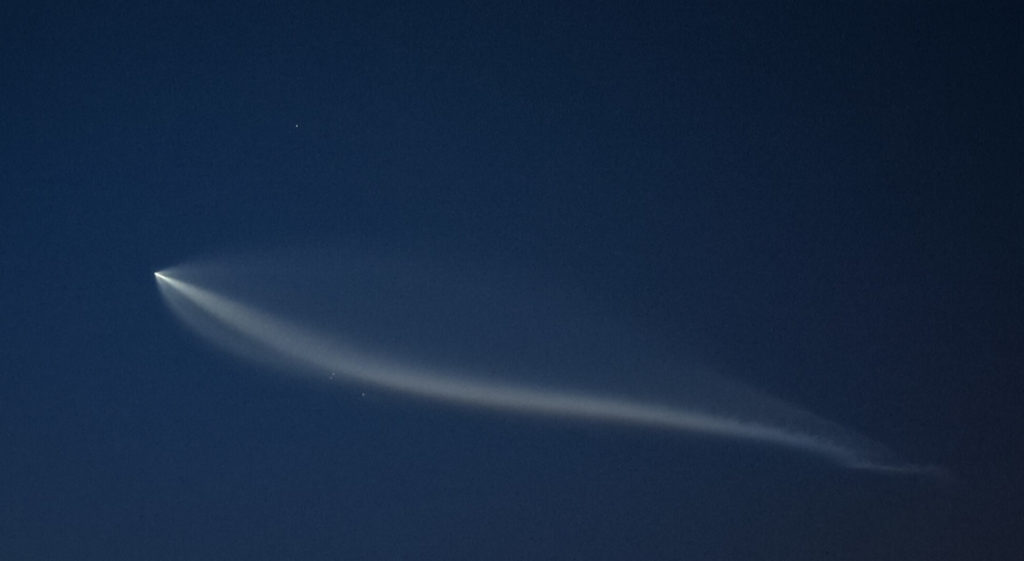 Falcon 9 rocket plume.  Faintly visible are the two fairing halves and the first stage booster.  Mars is in the background above the plume.