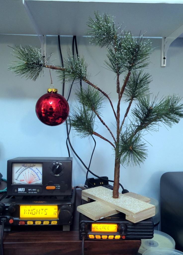 A Charlie Brown Christmas tree sitting on top of two radios in the shack.