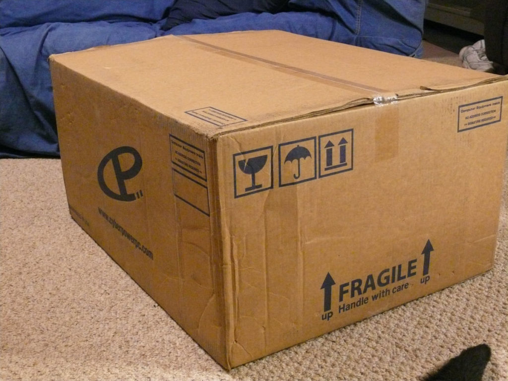 A large cardboard box sitting on the floor.  The box contains my new computer.
